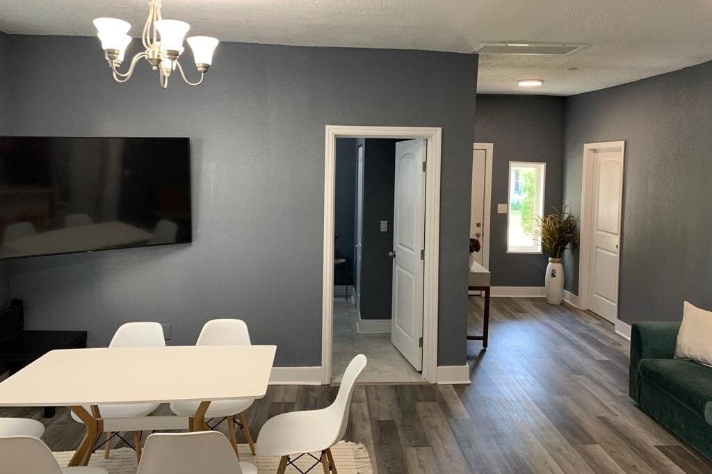A modern living room with a dining area, grey walls, and a chandelier.