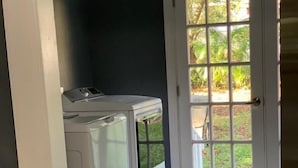 A laundry room with a front-loading washer and dryer, a trash can, and a door leading to a garden. - Fresh Home near Ybor city  (Tampa)