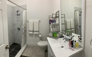 A bathroom with a shower, toilet, and a vanity with a mirror and shelves.