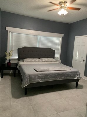 A bedroom with a bed, a nightstand, a ceiling fan, and a window with blinds.