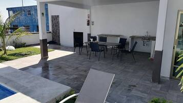 En utomhusplats med en uteplats, en pool, ett bord med stolar, en brandsläckare och en liten trädgård.