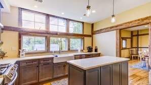A spacious kitchen with wooden cabinets, a large island, and a view of the outdoors through large windows. - The Lodge at Stoneleigh (Round Hill)