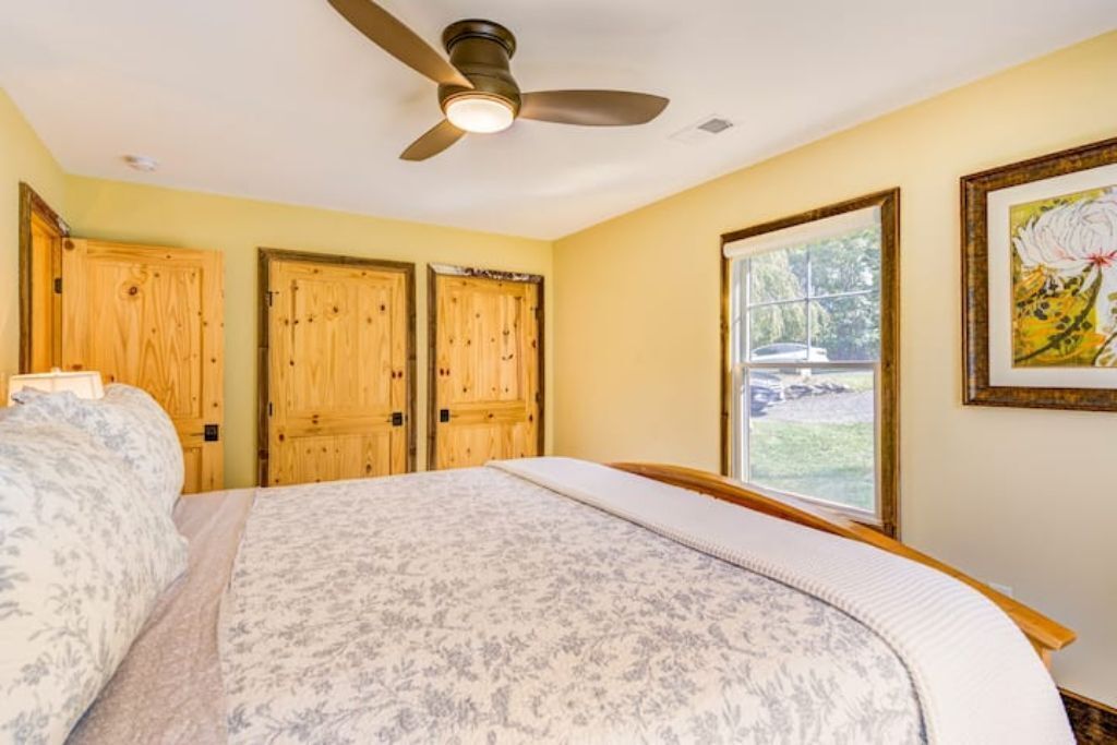 Quarto com cama, portas de madeira, ventoinha no teto e janela com vista para o exterior.