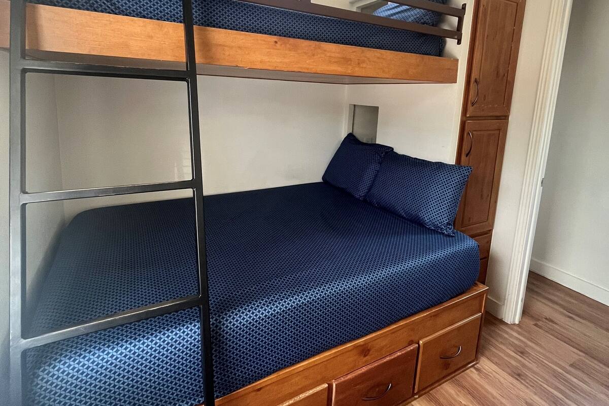 A bunk bed with a wooden frame and drawers, a ceiling fan, and a window with a view.