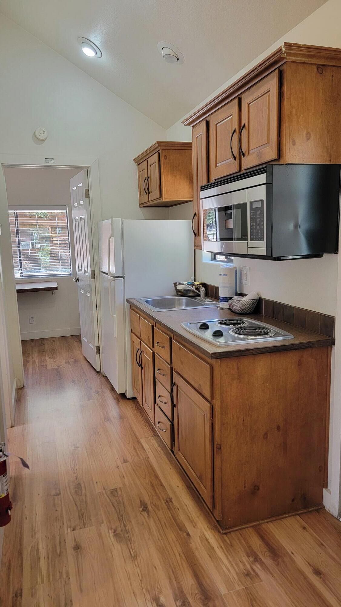 A kitchen with wooden cabinets, a stainless steel refrigerator, a microwave, and a stove.