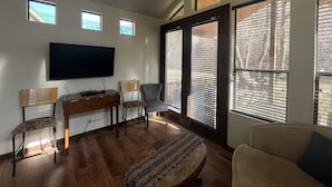 Un salon doté d’un téléviseur à écran plat, de meubles en bois et de grandes fenêtres équipées de stores.