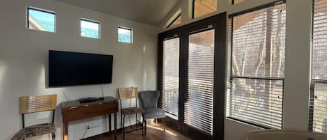 Un salón con televisor de pantalla plana, muebles de madera y ventanas amplias con persianas.