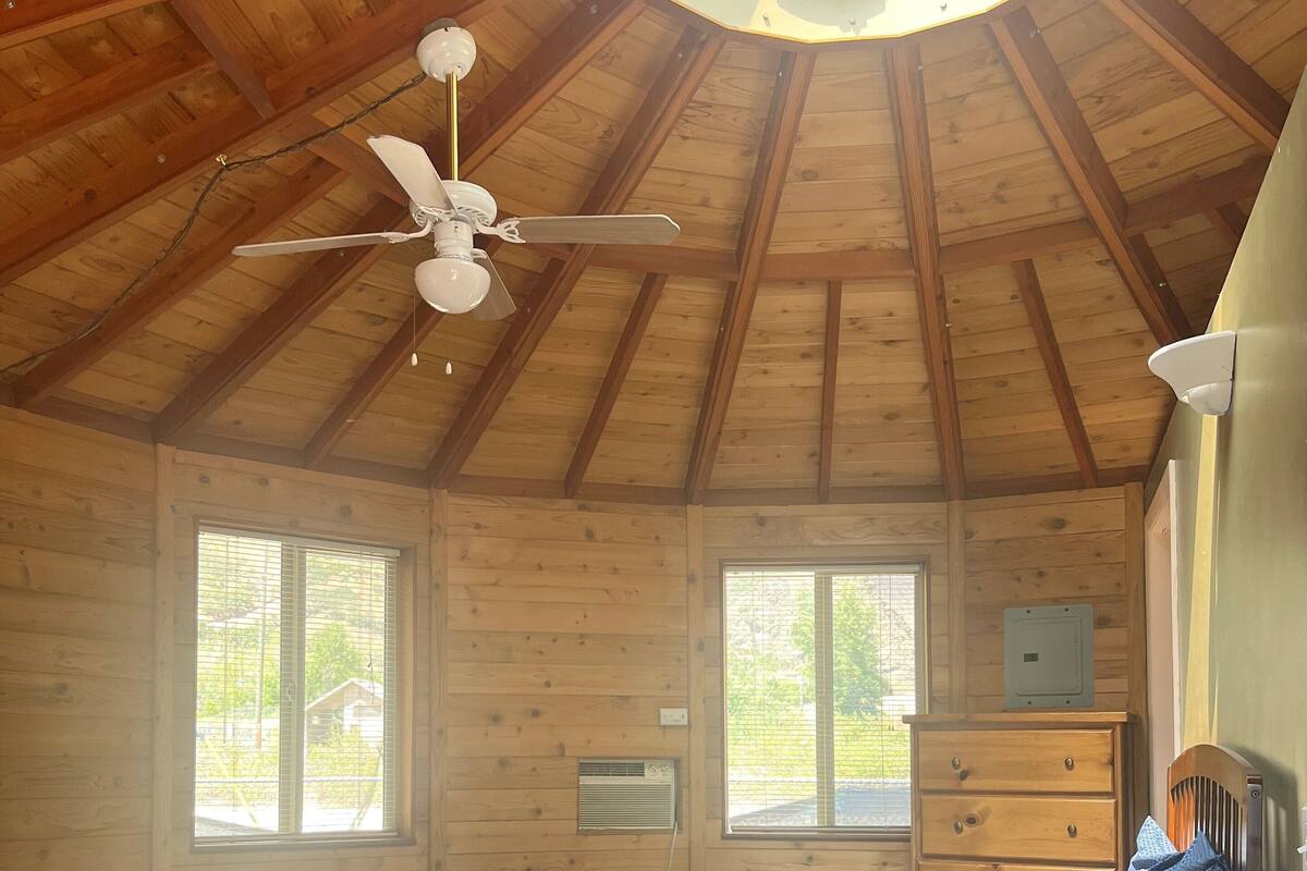 A wooden cabin bedroom with a bed, dresser, and a ceiling fan.
