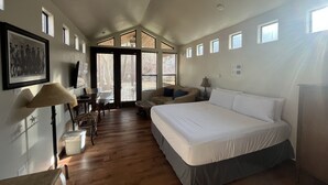 Une chambre spacieuse avec un grand lit, un bureau avec une chaise et un coin repas. De nombreuses fenêtres laissent entrer la lumière naturelle.