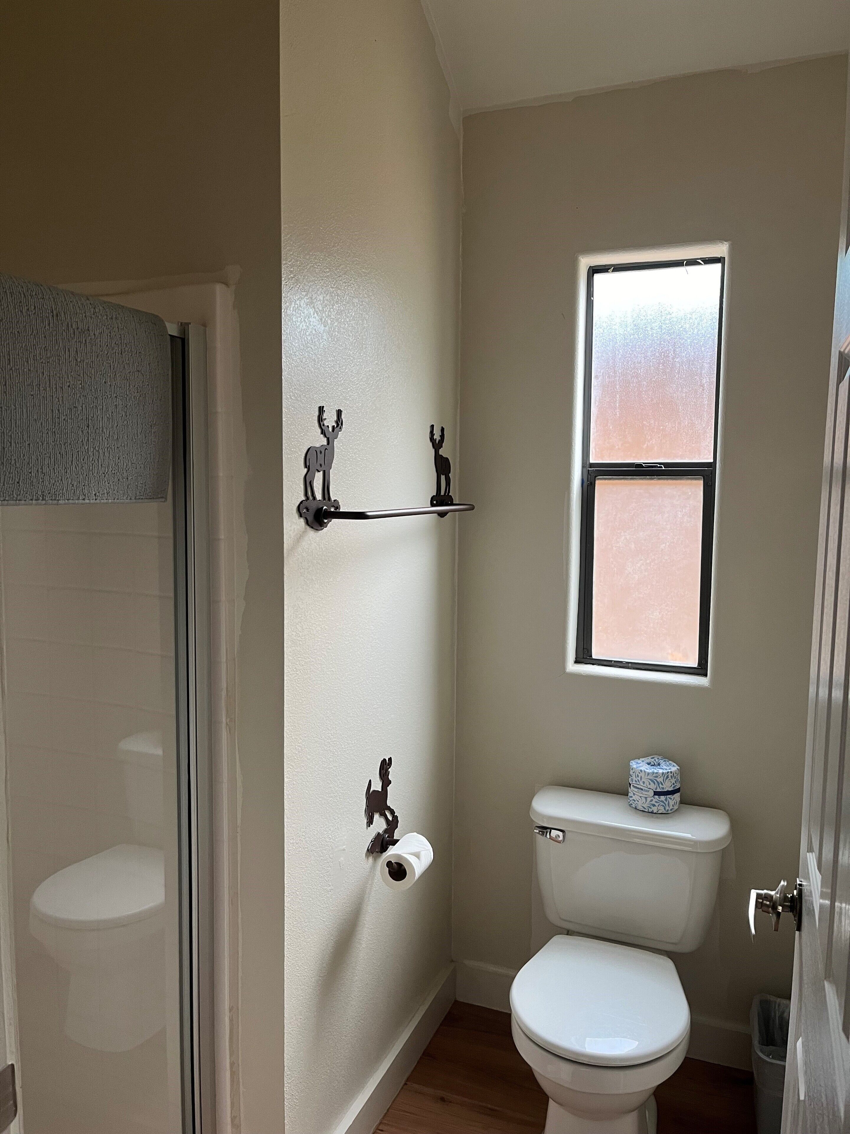 Un baño con inodoro, ventana y un perchero con forma de ciervo.