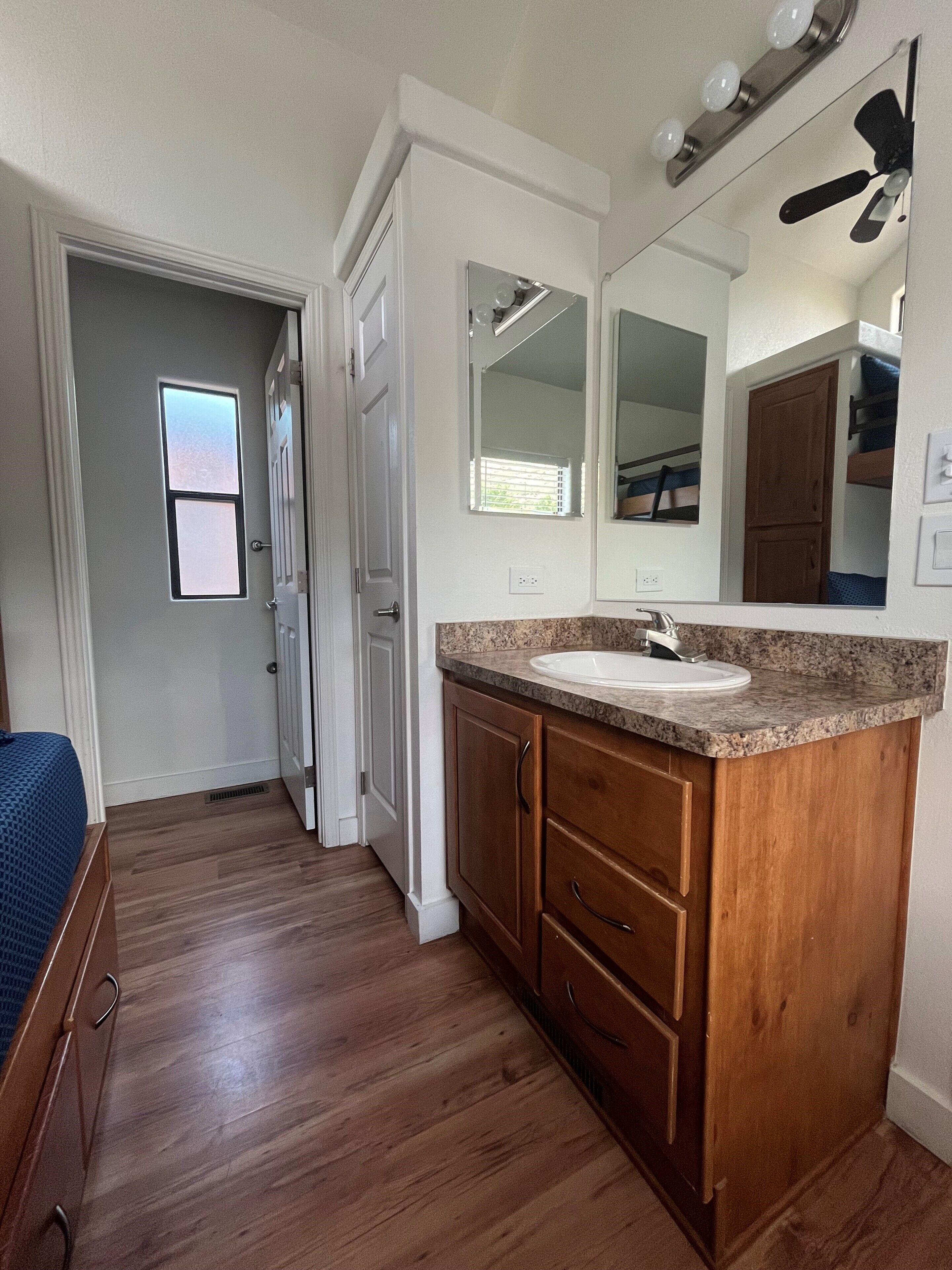 A bathroom with a vanity, sink, mirror, and ceiling fan.