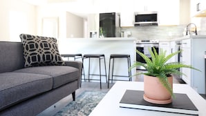 Una sala de estar moderna con un sofá gris, un cojín estampado y un helecho en maceta sobre una mesa blanca.