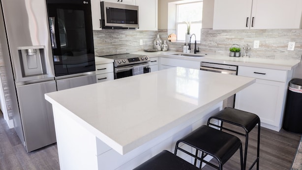 Una cocina moderna con armarios blancos, electrodomésticos de acero inoxidable y una isla grande con taburetes de bar.