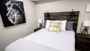 Una cama bien hecha con edredón blanco, cabecera de madera y dos lámparas de noche.