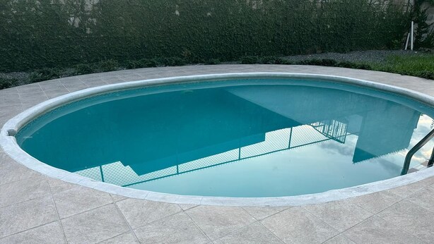 Ein Schwimmbecken mit Fliesen umrandet, umgeben von einer Hecke und einer Steinmauer.