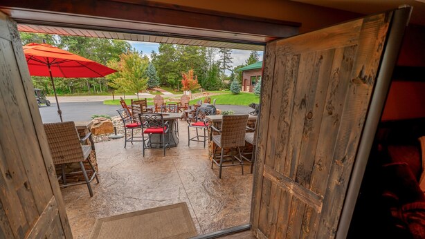 An open door leading to an outdoor patio with a table and chairs, a red umbrella, and a view of a road and trees. - Great outdoor entertainment with slip on Cross Lake (Crosslake)