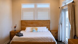 A bedroom with a wooden bed, two bedside tables, a nightstand, a lamp, and a window with curtains. - Stunning Ocean Views, Sleeps 10, New Build, Beach! (Flagler Beach)