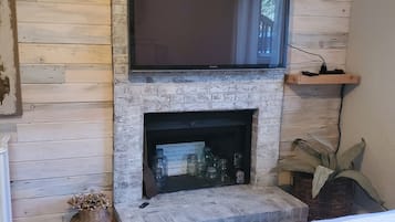 Una habitación con chimenea de piedra, televisor de pantalla plana montado encima y cama con manta color beige.