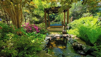 A garden with a wooden gazebo, a small pond, and lush greenery.