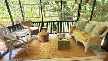 A cozy porch with wicker furniture, a woven mat, and a view of lush greenery.