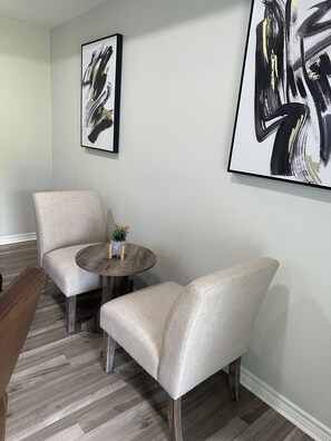 Un salon avec deux fauteuils, une petite table ronde et deux tableaux abstraits accrochés au mur.