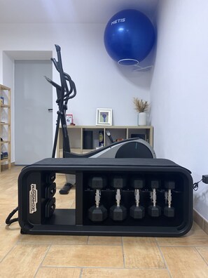 Ein Heimfitnessraum mit einem Ergometer, einem blauen Gymnastikball und Hanteln.
