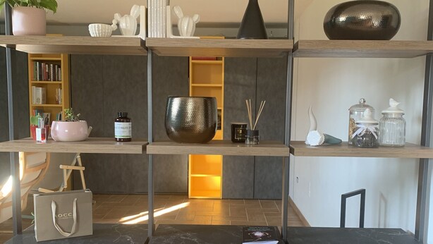Un interior modern amb sòcols de marbre, una estanteria de fusta amb diversos objectes decoratius i una taula petita amb un llibre i una ampolla.