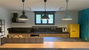 Una cuina moderna amb una illa central, llums penjants, forn encastrat i un frigorífic groc antic.
