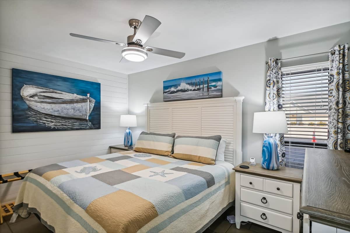 A bedroom with a bed, nightstands, a ceiling fan, and artwork on the walls.