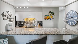 A modern kitchen with white cabinets, a granite countertop, and a clock on the wall. - Endless Summer By Book That Condo (Panama City Beach)
