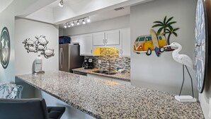 A modern kitchen with granite countertops, white cabinets, and a unique wall decoration featuring a van and a palm tree. - Endless Summer By Book That Condo (Panama City Beach)