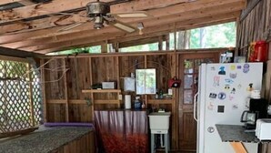 A rustic kitchen with wooden walls, a ceiling fan, a refrigerator, and a sink. - Plush Yome Tucked in the Woods (Monticello)