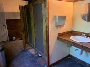 Un baño con puerta de madera, un lavabo blanco y un espejo.