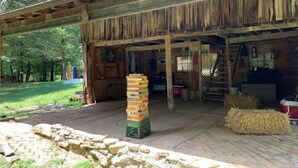 A rustic wooden building with a covered porch, a stack of wooden blocks, hay bales, and a stone wall. - Plush Yome Tucked in the Woods (Monticello)