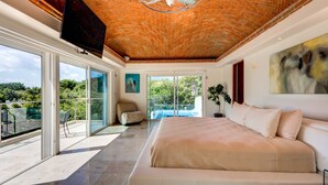 A bedroom with a large bed, a TV mounted on the wall, and a ceiling fan. - Casa Los Charcos
 (Playa del Carmen)