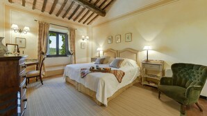 A bedroom with a large bed, bedside tables, a green armchair, a wooden desk, and a window with curtains. - Stunning private villa with private pool, WIFI, A/C, TV, pets allowed and panoramic view (Terriccio)