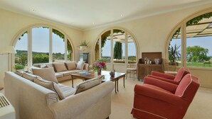 A spacious living room with a beige sofa, a red armchair, and a dining area with a table and chairs. Large arched windows provide a view of the outdoors. - Stunning private villa with private pool, WIFI, A/C, TV, pets allowed and panoramic view (Terriccio)