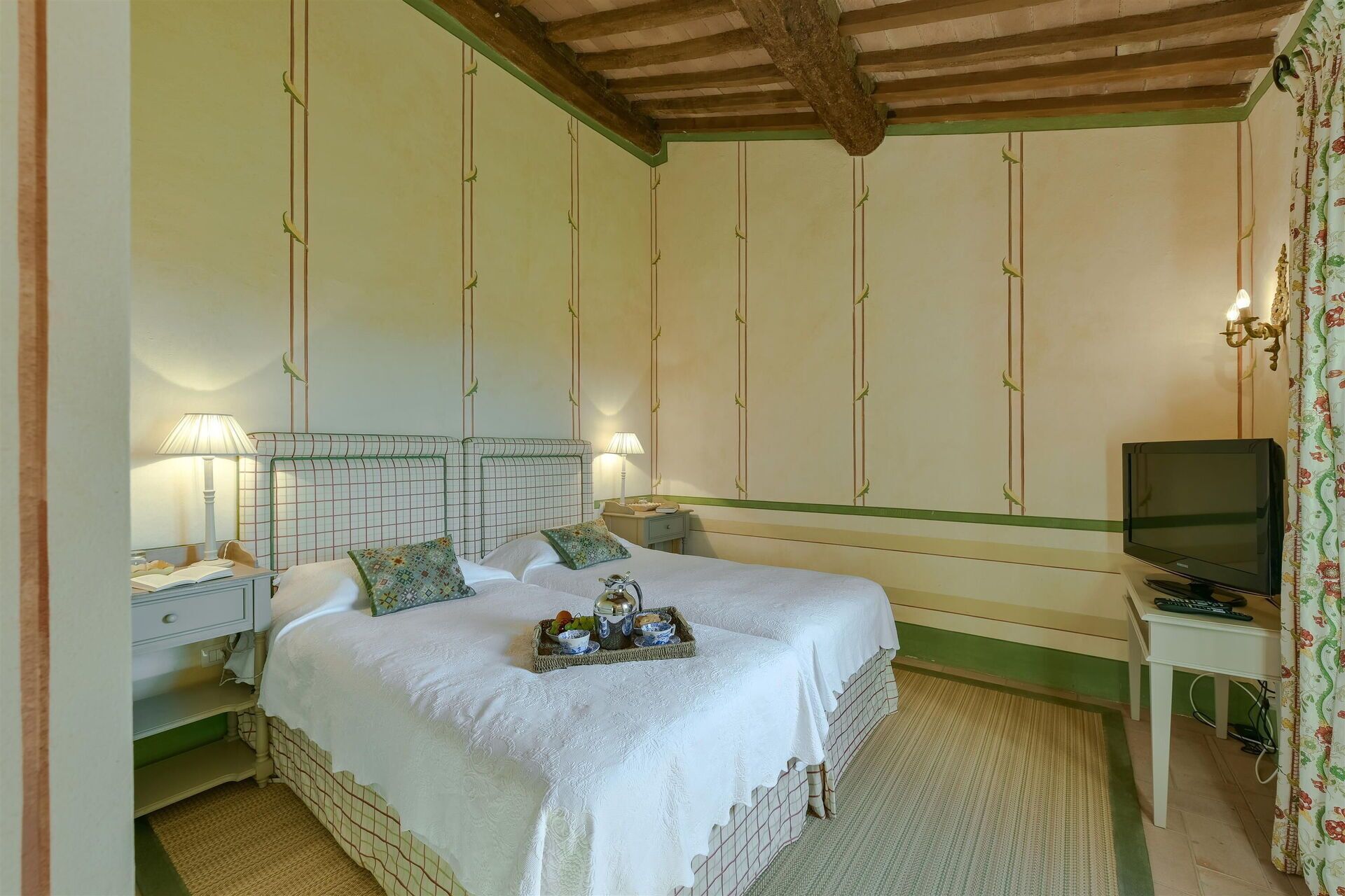 Een slaapkamer met twee bedden, een televisie en een klein tafeltje met een fruitschaal.