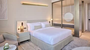 Una habitación de hotel moderna con una cama grande, mesitas de noche, una silla y una pequeña mesa con un jarrón.
