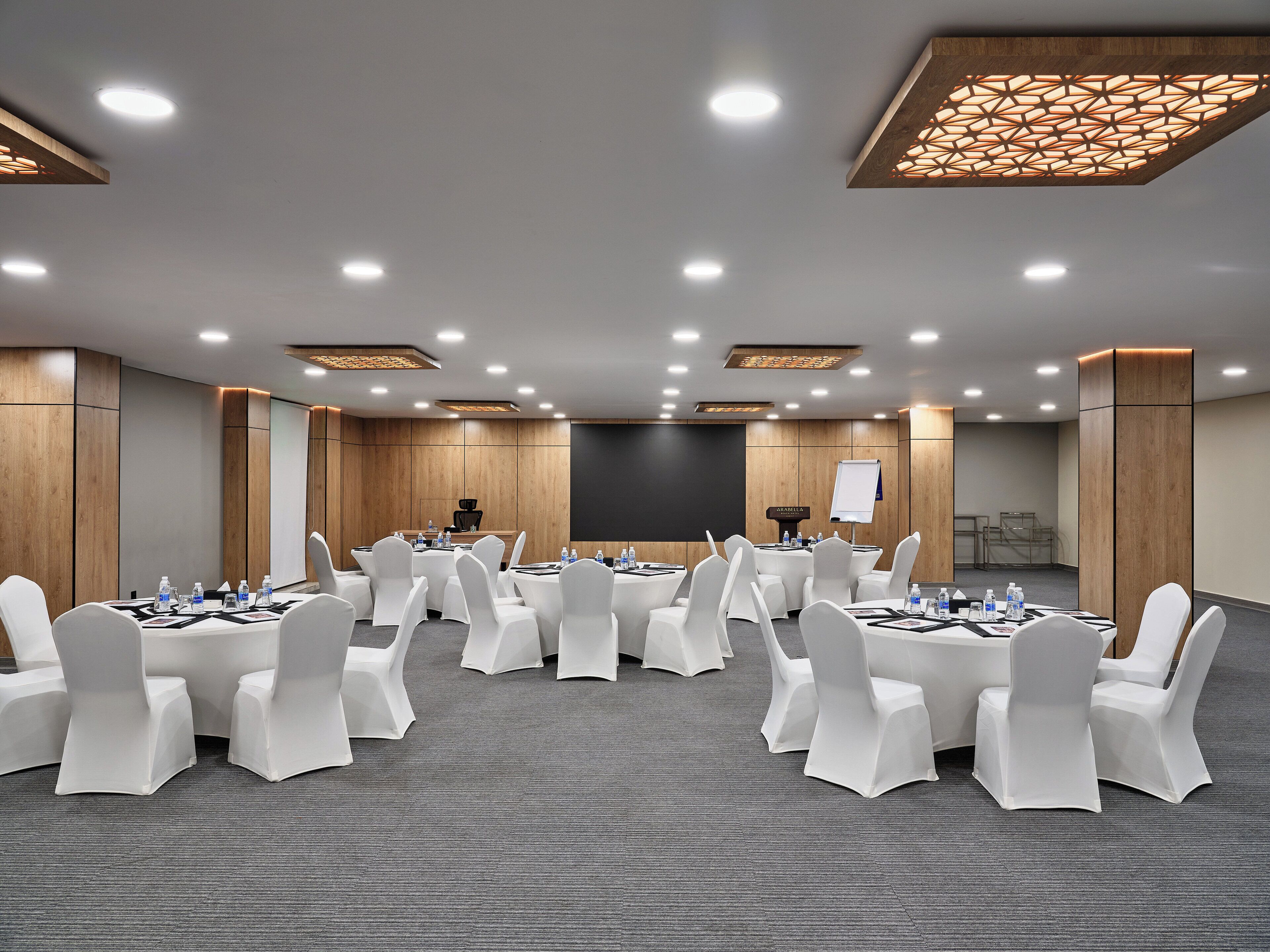 A conference room with round tables, white chairs, and a presentation screen.