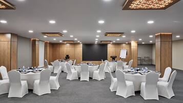 Un salón de conferencias con mesas redondas, sillas blancas y una pantalla para presentaciones.