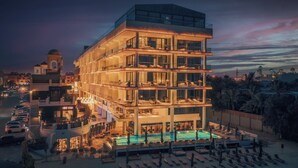 Een meerhoog hotel met een zwembad, balkons en uitzicht op de omliggende stad.
