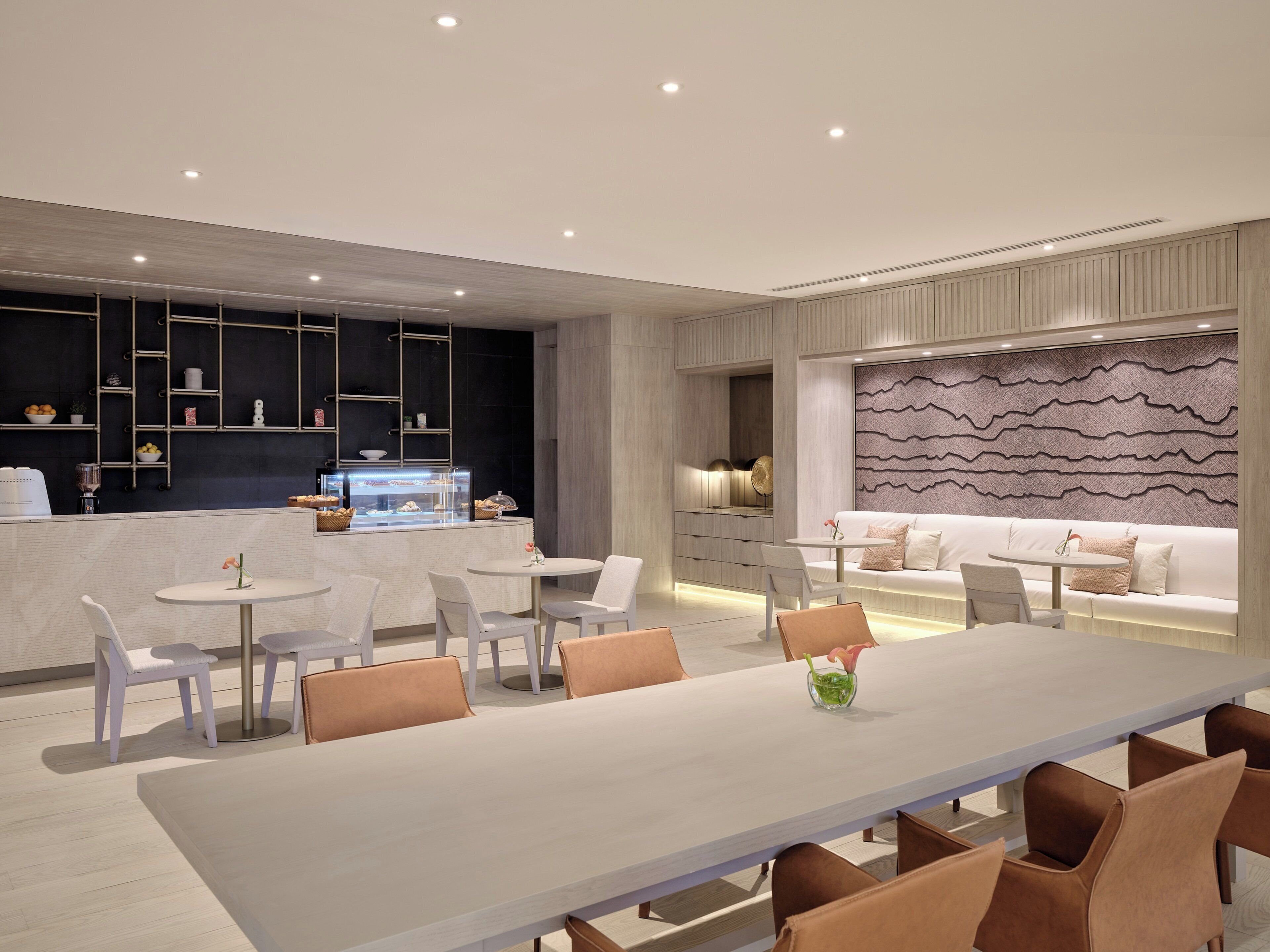 A modern dining area with a long table and chairs, a counter with a display case, and a seating area with a sofa and cushions.
