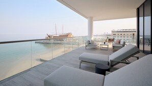 Een modern balkon met lounge fauteuils, een tafel en uitzicht op een schip en stadsbeeld.