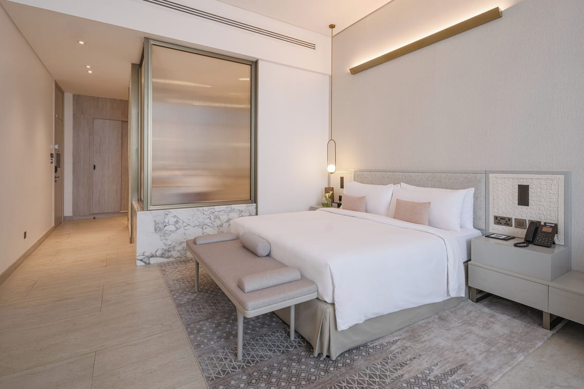 A modern hotel room with a large bed, bedside table, and a bench.