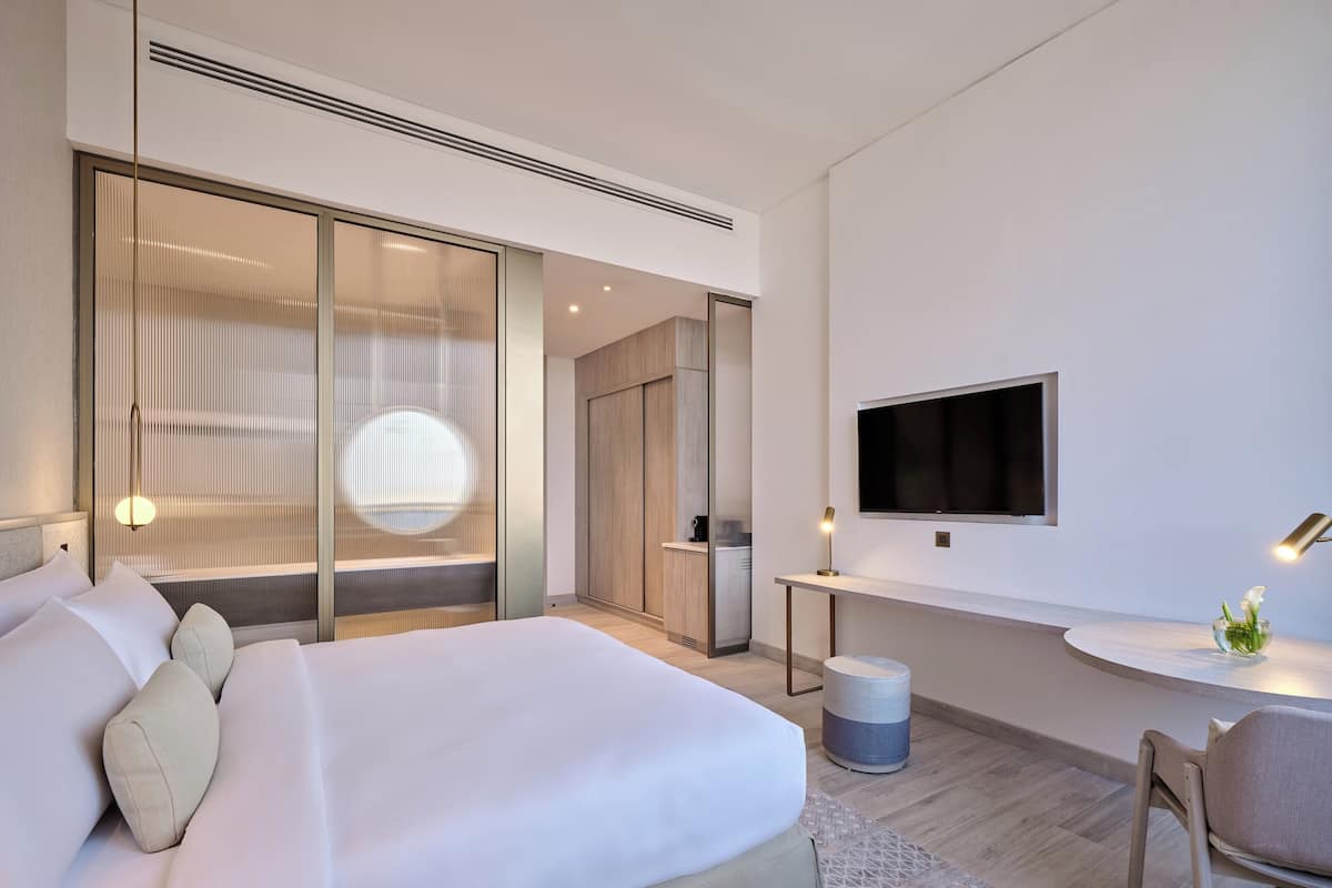 A modern hotel room with a large bed, a TV mounted on the wall, and a desk with a chair.