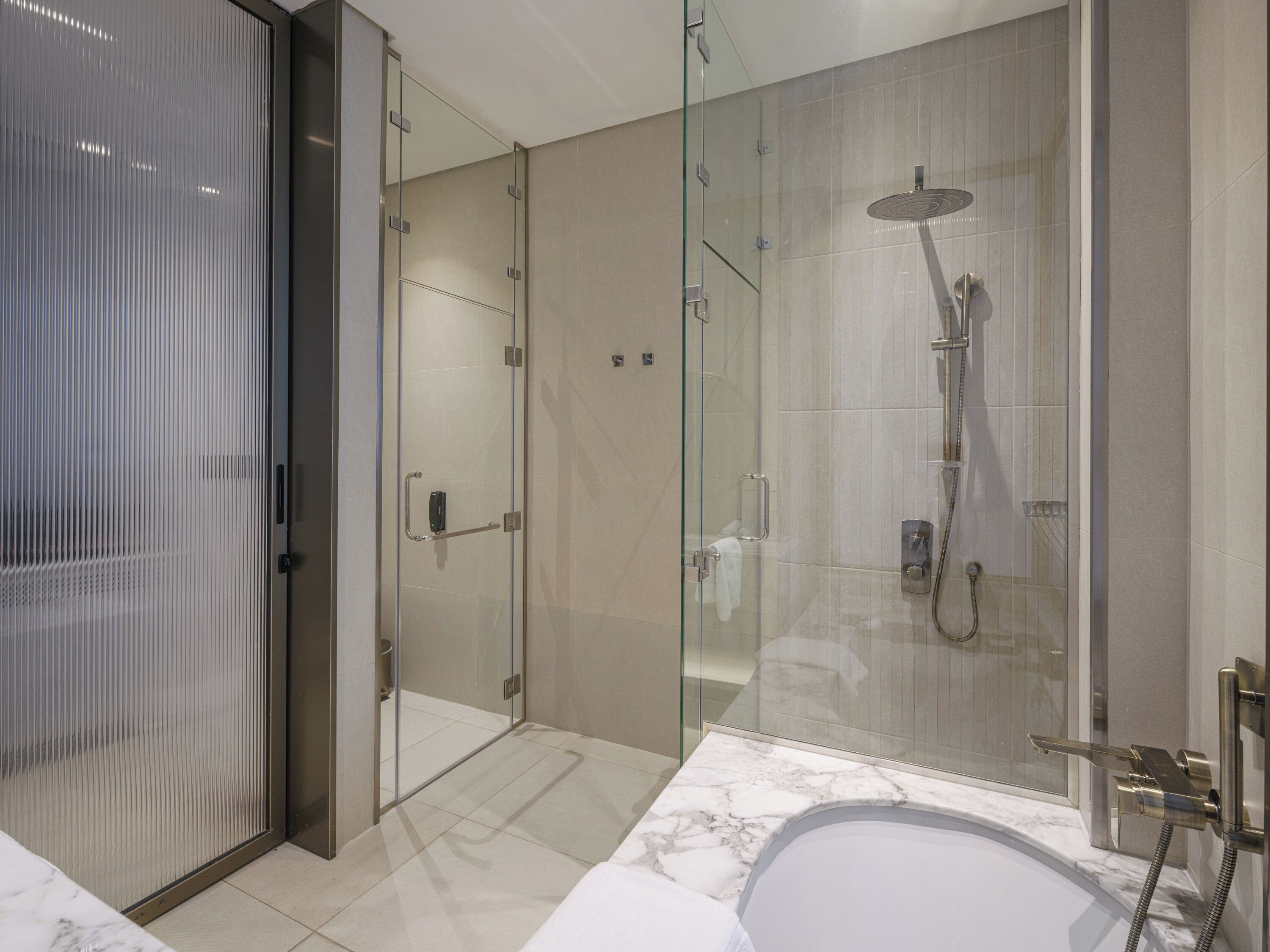 Ein modernes Badezimmer mit einer Duschkabine aus Glas, einem Marmorwaschbecken und einer Glastür zu einem weiteren Raum.