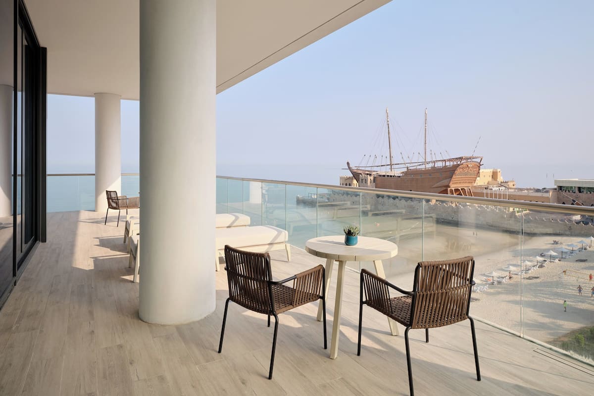 A balcony with a view of the sea and a ship. There are chairs and a table.