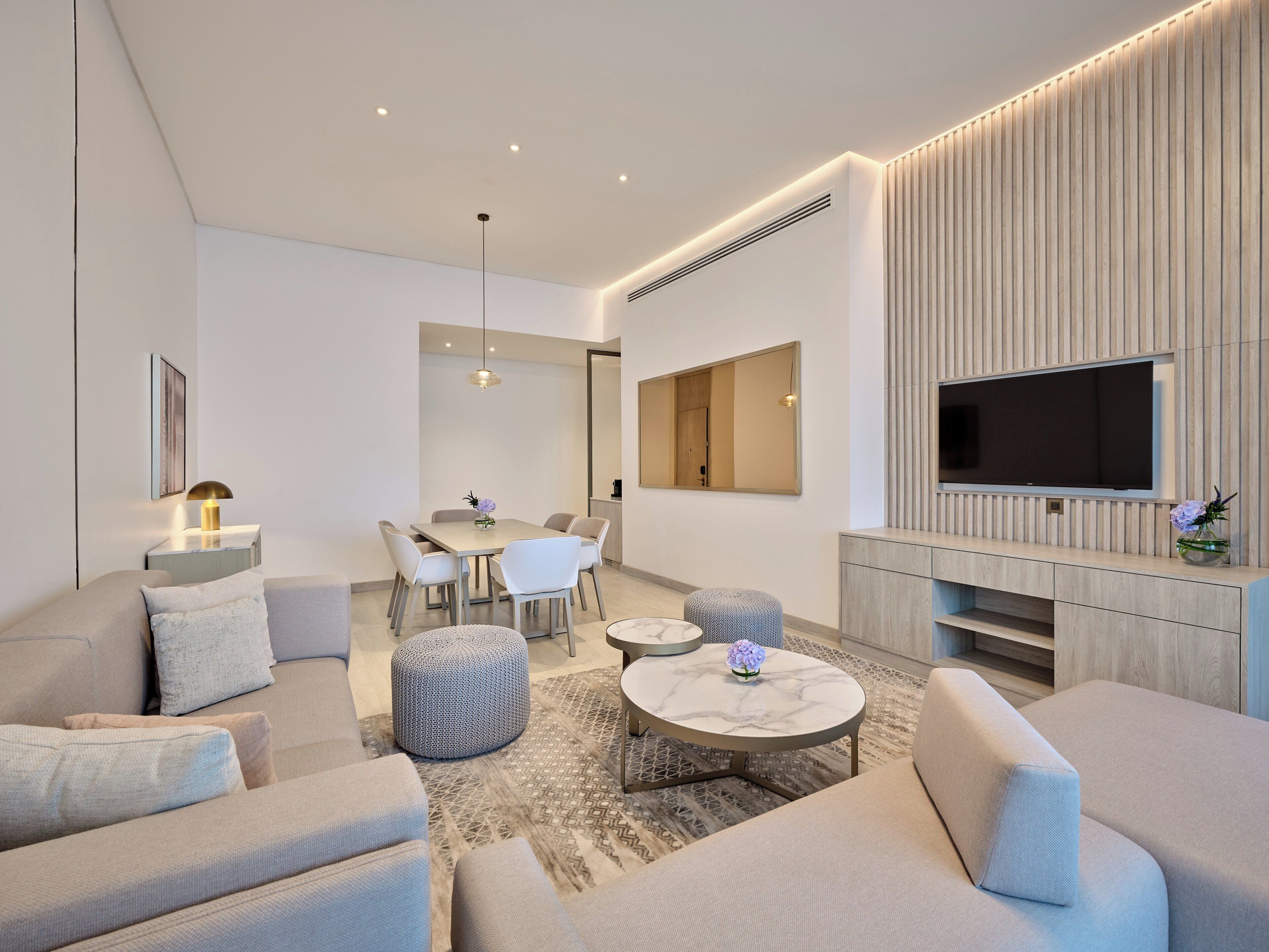A modern living room with a sofa, ottoman, coffee table, and a flat-screen TV mounted on a wooden wall.