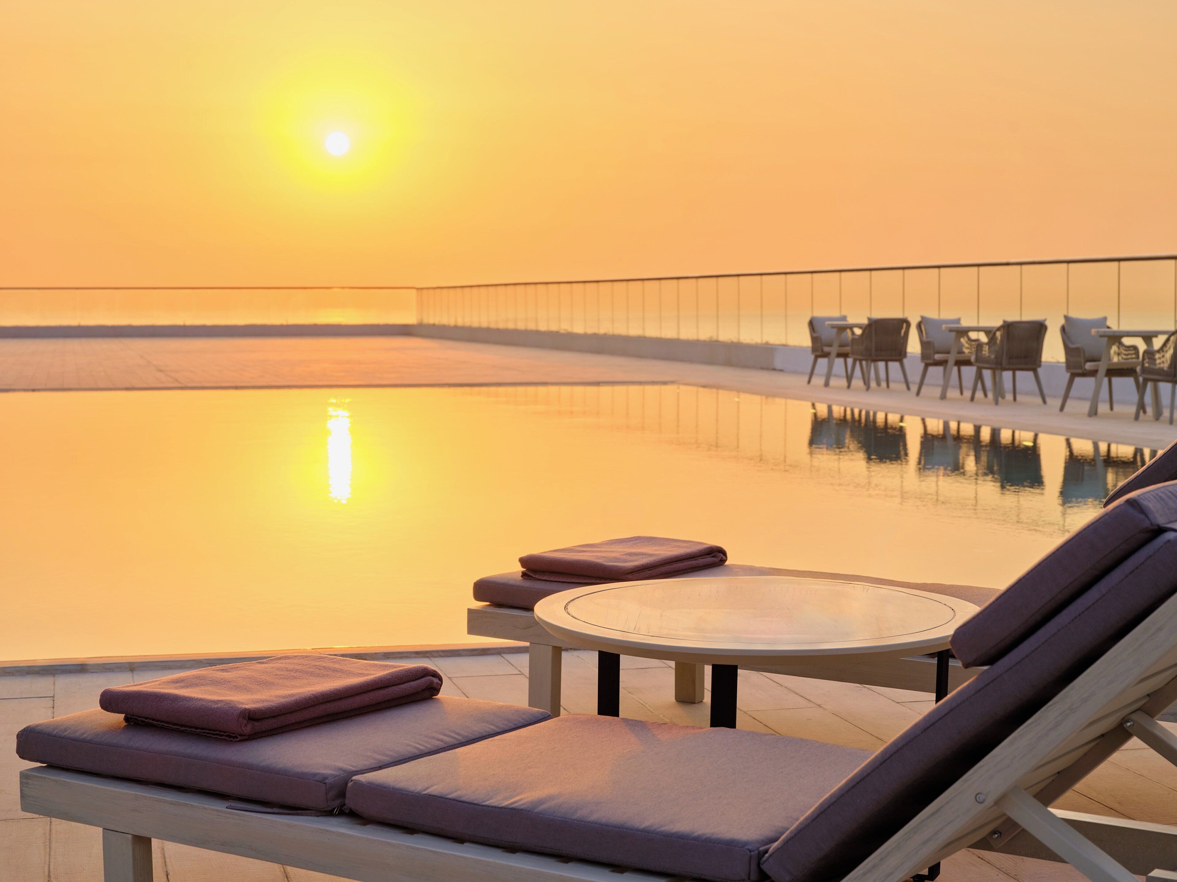 A poolside area with lounge chairs and a table, surrounded by a glass railing.